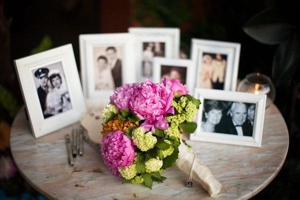 Bride's dark pink, orange, yellow, and green bouquet on table with wedding portraits of the bride and groom's family in the background - photo by Orange County based wedding photographers Mark Brooke